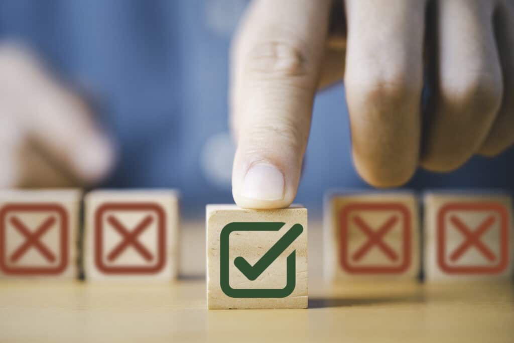 Hand is pushing a green correct sign symbol in front of a Red Cross sign on a wooden block cube for Choosing the Right Water Heater by Benjamin Franklin Plumbing of Myrtle Beach, SC.