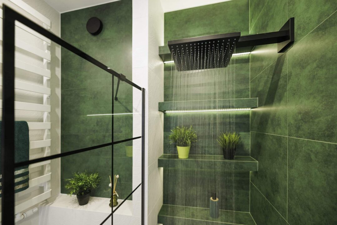 After the shower remodel, water cascades from a black rain shower head in a luxurious green bathroom.