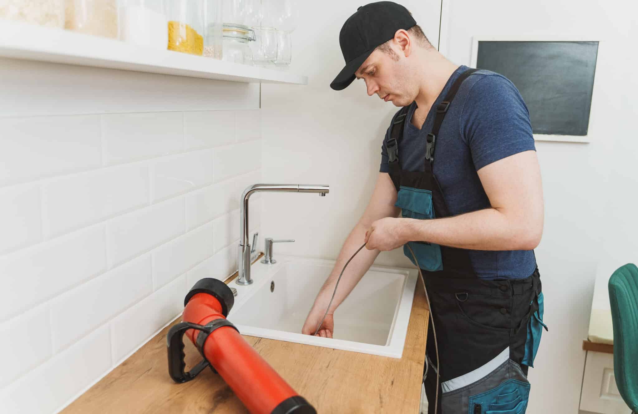Plumber using drain snake drain clogs.
