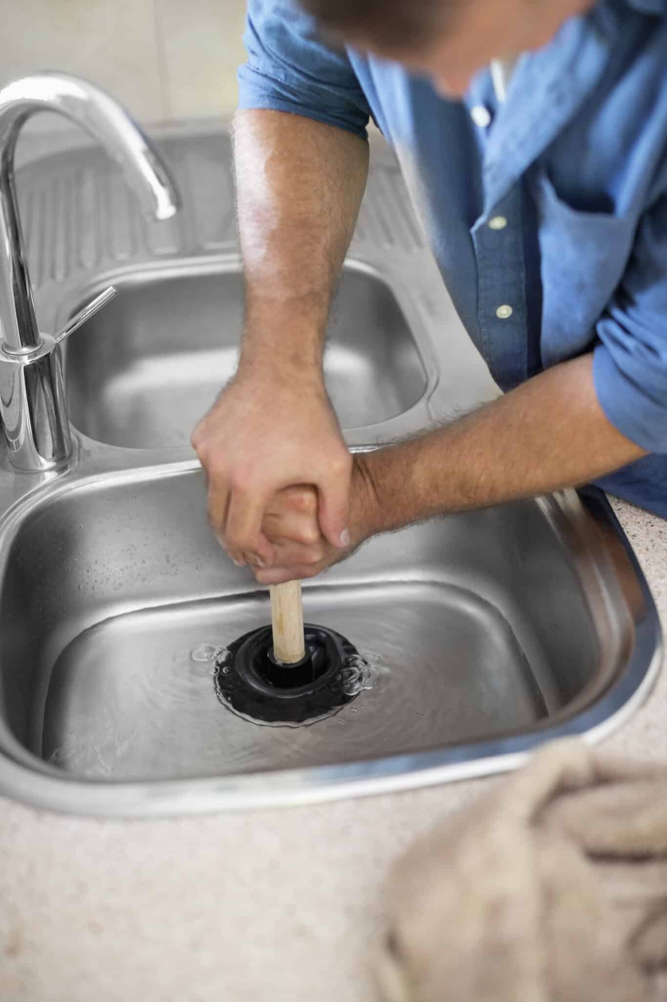 Plumber unclogging kitchen sink using plunger, Common Plumbing Failures.