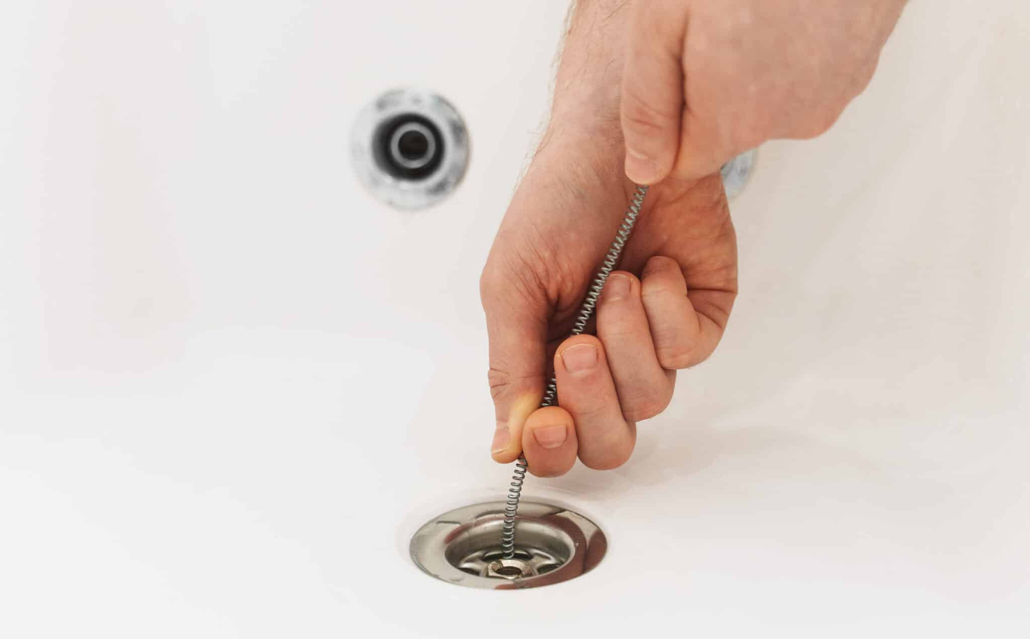 Plumber using drain snake to unclog bathtub, Rooter Service.